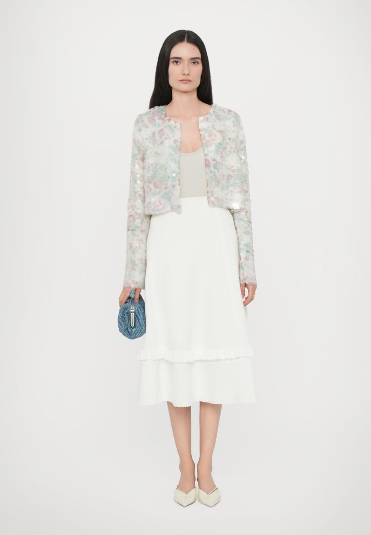 Veste à sequins floraux dans des couleurs pastel, débardeur beige, jupe blanche à volants, sac à main en tissu texturé bleu et ballerines crèmes à bout pointu.