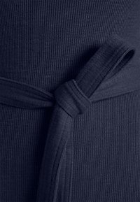Gros plan d'une ceinture en tissu côtelé bleu foncé nouée en un simple nœud autour d'un vêtement à texture assortie.