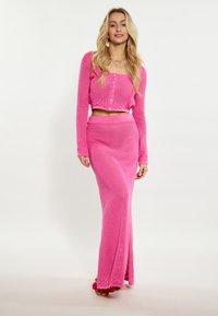 Háčkovaný dvojdielny outfit v jasnej ružovej farbe. Obsahuje dlhé rukávy, skrátený top s gombíkmi a maxi sukňu s textúrovaným vzorom.