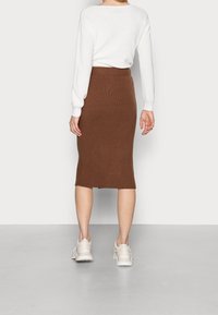 Hnědá žebrovaná midi sukně s dobře padnoucím pasem a mírně rozparkem na lemu, spárovaná s krémovým svetrem a světle barevnými teniskami.