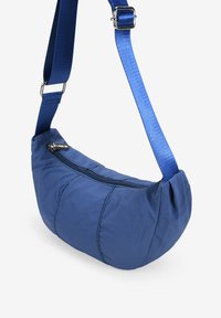 Bolso de hombro de nylon azul con forma curva, cierre con cremallera y correa ajustable. Superficie texturizada con costuras visibles.