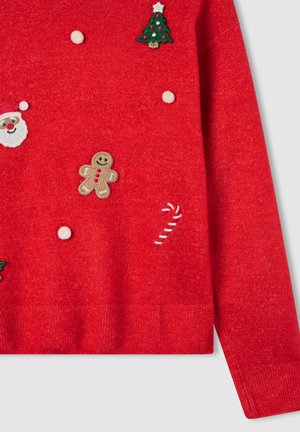 Maglione rosso lavorato a maglia con ricami a tema festivo: albero di Natale, Babbo Natale, omino di pan di zenzero, bastoncino di zucchero e pompon bianchi.