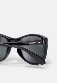 Mustad musta Polaroidi päikeseprille hallide polariseeritud läätsedega, millel on sujuv ovaalne disain ja eristuv logo varrela, sile tekstuur kogu ulatuses.