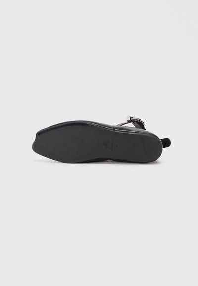 Black flat-soled shoe with a smooth leather upper and an ankle strap. The sole has a slight curve, featuring minimal branding and no visible patterns.