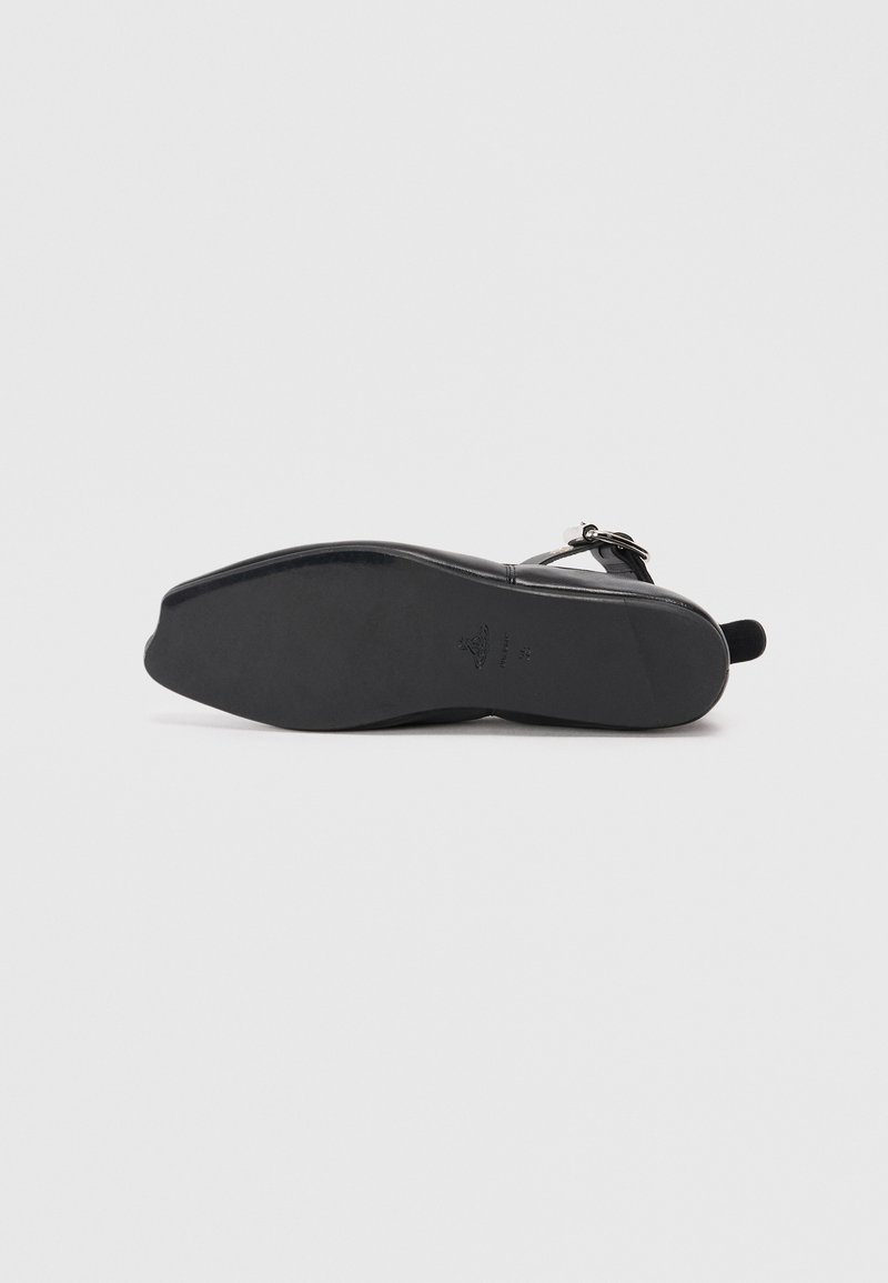 Chaussure noire à semelle plate avec un dessus en cuir lisse et une bride à la cheville. La semelle présente une légère courbure, avec un marquage minimal et sans motifs visibles.