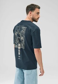 Navy blue cotton t-shirt featuring a detailed white graphic print on the back with text and waves design, short sleeves, and relaxed fit.