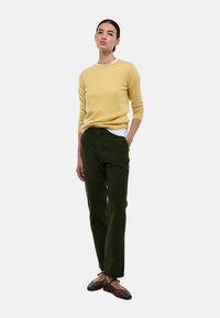 Pull jaune, pantalon en velours côtelé vert et chaussures en tissu tressé marron. Le pull a un col rond ; le pantalon présente un côtelé vertical ; les chaussures ont des détails découpés.