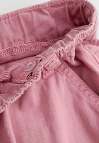 Bawełniany pas w jasnoróżowym kolorze, z marszczoną teksturą, z zapięciem na guzik oraz widocznymi detalami szycia wzdłuż krawędzi.