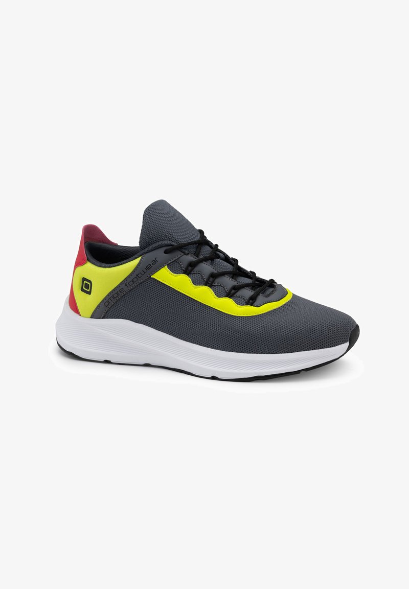 Grau sportlicher Schuh mit schwarzen Schnürsenkeln, gelben Akzenten und einer strukturierten Oberfläche. Verfügt über eine weiße Sohle und eine rote Fersenschlaufe.