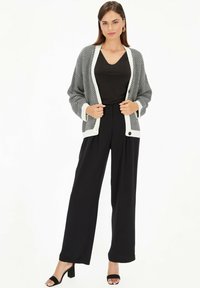 Czarny i biały kardigan w wzór rybiej ości z kontrastowym kołnierzem, zestawiony z czarnymi spodniami o szerokich nogawkach i czarnymi sandałami na obcasie.