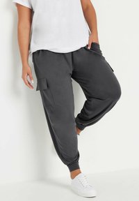 Grå, löst sittande cargobyxor i sweatshirtmaterial med elastiska muddar och sidfickor, tillsammans med en vit t-shirt och vita sneakers.