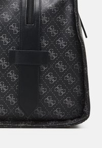 Borsa in ecopelle nera con motivo a logo impresso, dotata di chiusura con zip e tracolla piatta. Superficie testurizzata e design angolare.