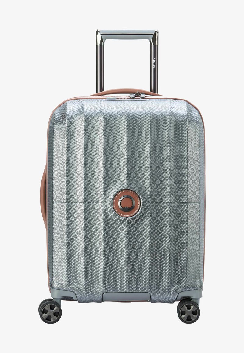 Valise rigide avec une surface texturée argentée, des accents en rose gold, une poignée extensible et quatre roues noires pour la mobilité.