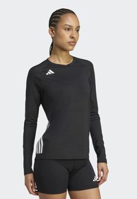 Černé sportovní tričko s dlouhým rukávem a reflexními pruhy na rukávech, kombinované s těsnými černými šortkami. Hladká látka, moderní design.