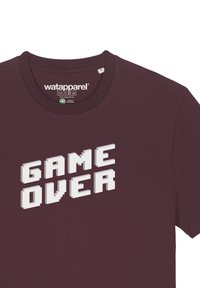 Bordeaux T-shirt met een witte, pixelachtige "GAME OVER"-grafiek. De stof lijkt zacht met een ronde halslijn en korte mouwen.