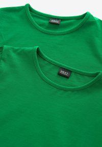 Deux t-shirts en coton verts empilés, présentant des encolures rondes avec des bords cousus et des étiquettes noires dans la zone intérieure du col.