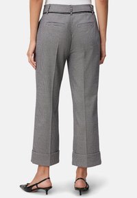 Bagudsig af mønstrede bukser i sort og hvid houndstooth, med en afslappet pasform, ankellang kant og to baglommer.