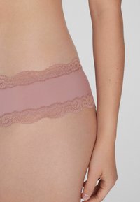 Růžové bezešvé kalhotky s jemným krajkovým pasem. Materiál je hladký a krajka má květinové vzory podél okrajů.