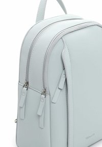 Helehall seljakott sileda tekstuuriga, kahe lukuga sahtlite ja lühikese sangaga. Omab peeneid õmbluse detaile ja logo.