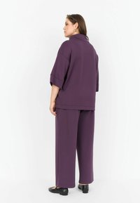 Set de lounge violet, realizat dintr-un material moale, care include un top lejer cu mâneci scurte și pantaloni cu o croială confortabilă. Încălțăminte plată neagră completează ținuta.