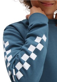 Blå långärmad t-shirt i mjukt tyg, med ett vitt rutmönster längs ärmarna och rund halsringning.