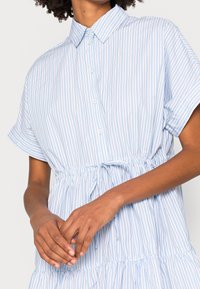 Niebieska i biała sukienka w paski z kołnierzykiem, krótkimi rękawami, pasem ze sznurkiem i warstwowym dołem. Lekki materiał.