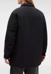 Zwarte gewatteerde jas met een losse pasvorm, voorzien van een puntige kraag, knoopmanchetten en een gladde matte textuur. Eenvoudig ontwerp zonder versieringen.