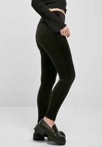 Czarne prążkowane legginsy mają wysoki stan z gładką fakturą. Połączone z masywnymi czarnymi butami typu slip-on dla uzyskania warstwowego wyglądu.