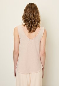 Bezrękawnik w jasnoróżowym kolorze z zaokrąglonym dekoltem z tyłu. Miękka, teksturowana tkanina i surowe krawędzie u dołu oraz przy dekolcie.