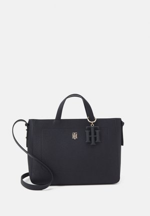 Bolso tote de cuero negro con textura de perlas, con dos asas superiores, correa de hombro extraíble, herrajes dorados y un colgante con las iniciales "H H".