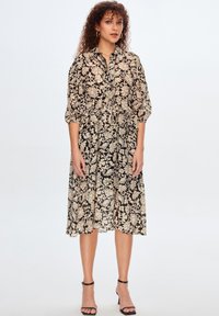Vestito floreale nero e crema con bottoni anteriori, maniche a tre quarti e vita sfiancata, realizzato in tessuto leggero.
