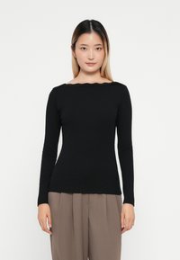 Top negro de manga larga con escote barco y borde festoneado, hecho de un tejido suave, combinado con pantalones de tiro alto beige.