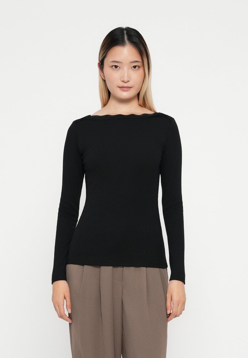 Top negro de manga larga con escote barco y borde festoneado, hecho de un tejido suave, combinado con pantalones de tiro alto beige.