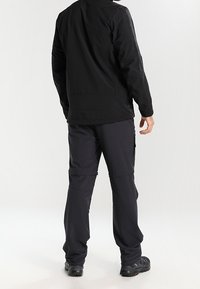 Veste noire résistante à l'eau avec un col montant, une coupe ajustée et des poches zippées, associée à un pantalon cargo sombre ajustable et des chaussures robustes.