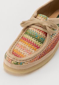 Chaussure en cuir beige avec dessus en textile tissé multicolore dans les teintes rose, verte et orange. Présente un bout arrondi et un laçage assorti.