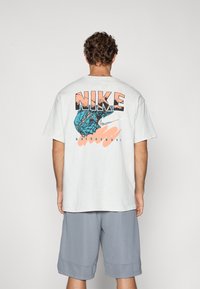 Lys grå bomulds T-shirt med et stort blåt og orange grafik på ryggen, med teksten "NIKE" og "BASKETBALL". Kortærmet.