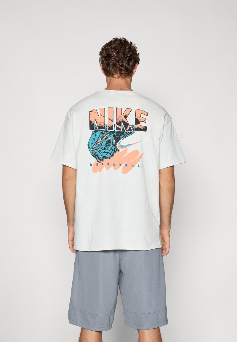 Lys grå bomulds T-shirt med et stort blåt og orange grafik på ryggen, med teksten "NIKE" og "BASKETBALL". Kortærmet.