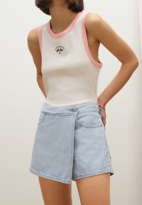 Vit linne med rosa detaljer och en logotyp. Ljusblå jeansshorts med omslag och knapp som visar en avslappnad stil.