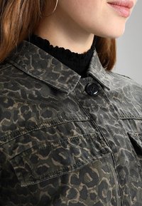 Camisa de estampado de leopardo verde, con cuello tipo solapa, cierre frontal de botones y dos bolsillos en el pecho con un tejido texturizado.