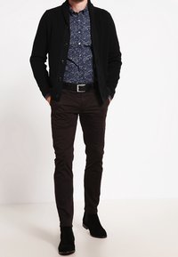 Schwarze Strickjacke über einem blauen, blumenbedruckten Hemd, kombiniert mit dunklen Hosen und schwarzen Knöchelstiefeln; verfügt über einen Knopfverschluss und strukturierten Stoff.