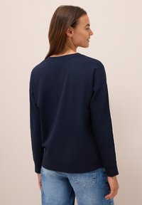 Sweatshirt bleu marine à manches longues, col rond et rayures blanches sur les côtés. Tissu doux avec une coupe décontractée, porté avec un jean bleu clair.