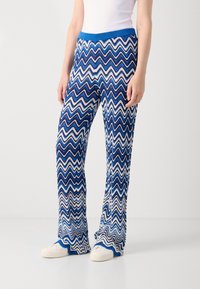 Blue and white zigzag patterned pants with a ribbed blue waistband, made of a soft fabric. Flared leg design with a textured finish.