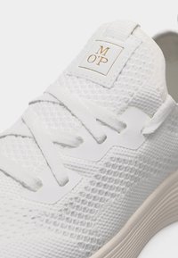 Λευκό πλεκτό αθλητικό παπούτσι με λευκά κορδόνια και ετικέτα στη γλώσσα με το κείμενο "M O'P" σε χρυσά γράμματα.