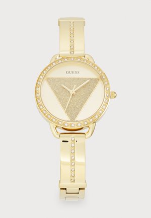 Montre dorée avec un cadran triangulaire scintillant, entouré d'une lunette accentuée de cristal et d'un bracelet lisse avec des maillons décoratifs.