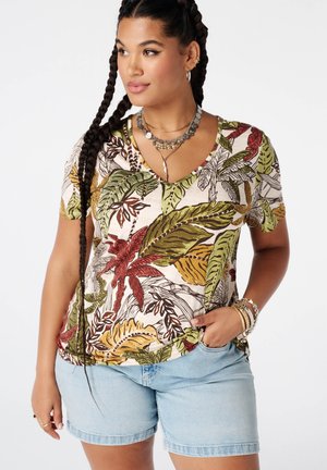 Vrouw met lang gevlochten haar die een kleurrijk shirt met tropische bladprint draagt, lichte denim shorts en gelaagde kettingen en armbanden.