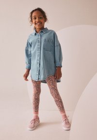Denim skjortekjole med en forlommer, kombineret med blomstrede leggings i blå og pink toner. Pinke sneakers med hvide såler og striber.