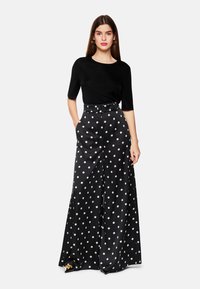 Schwarzes Kurzarmoberteil kombiniert mit hoch taillierten, schwarzen, weit geschnittenen Hosen mit großen weißen Punkten und einem taillierten Gürtel.