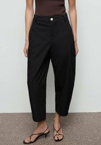 Pantaloni neri su misura con design a gamba dritta, dotati di chiusura con bottone visibile e tasche inclinate. Tessuto morbido con texture delicata.