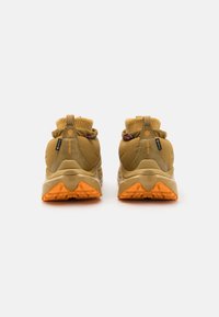 Scarpe da trekking tan con tomaia in tessuto testurizzato, colletto in maglia flessibile e suola arancione distintiva. Dotate di linguetta e dettagli di branding.