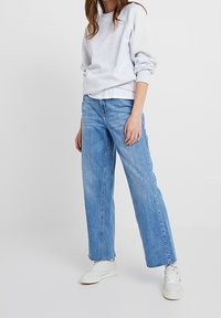 Světlě šedá mikina s kulatým výstřihem a žebrovanými manžetami, kombinovaná s volnými, vybledlými modrými džíny a bílými teniskami.